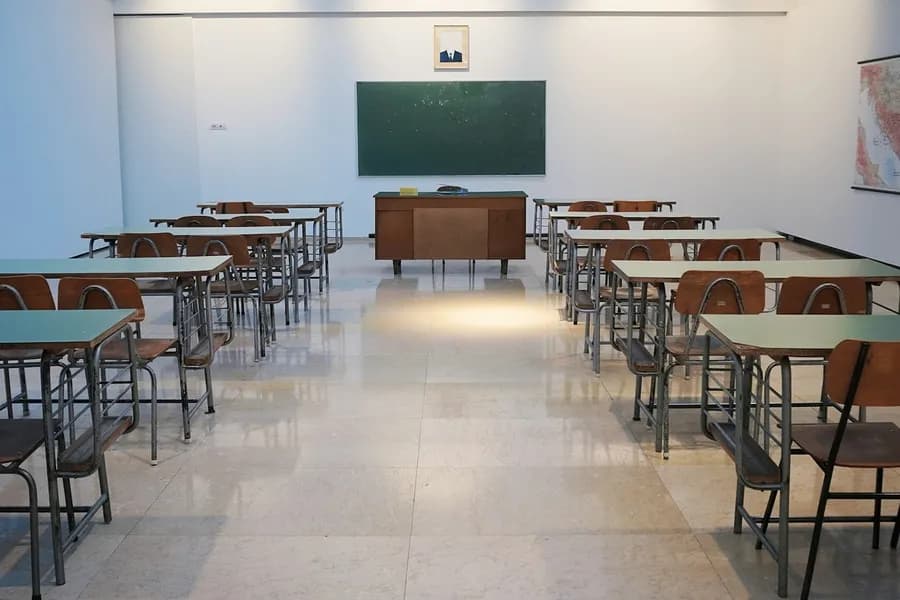A bright, empty classroom with rows of desks facing a green board