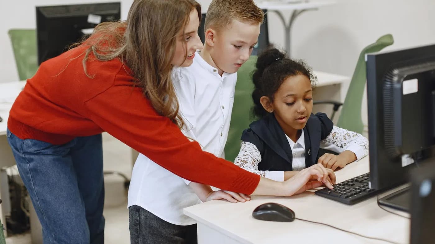A teacher helping two young pupils at a classroom computer