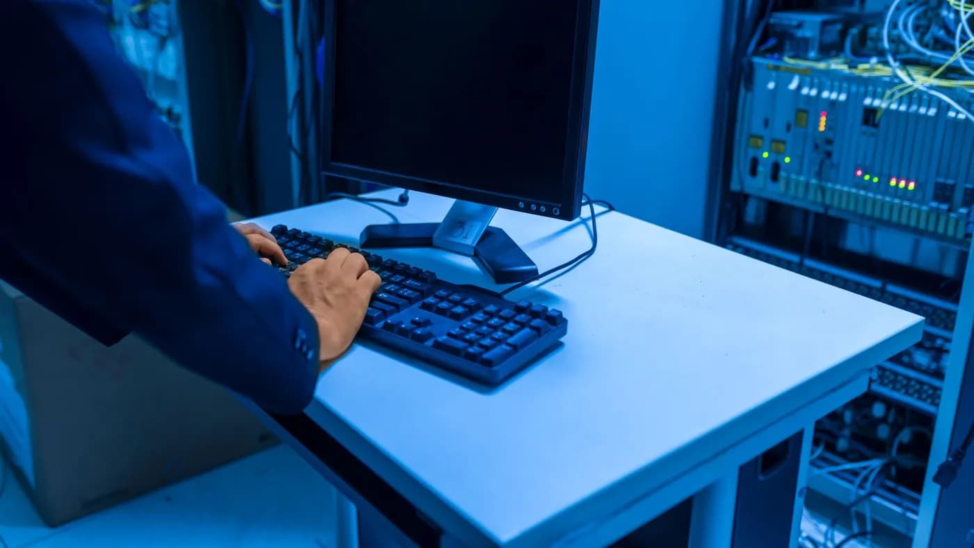 An IT professional at a keyboard beside a rack of network equipment