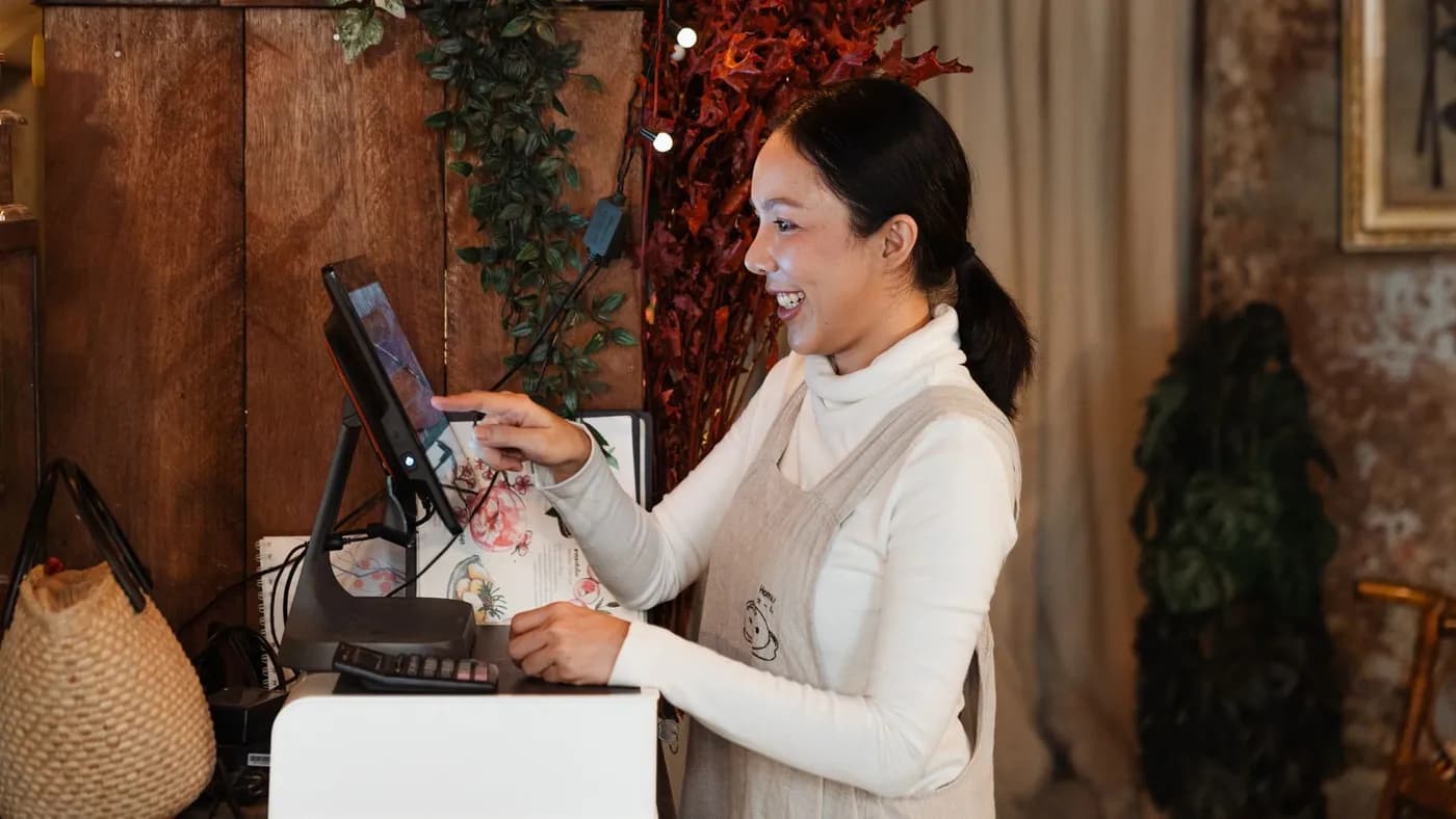 A shop owner smiling as she uses a touchscreen till