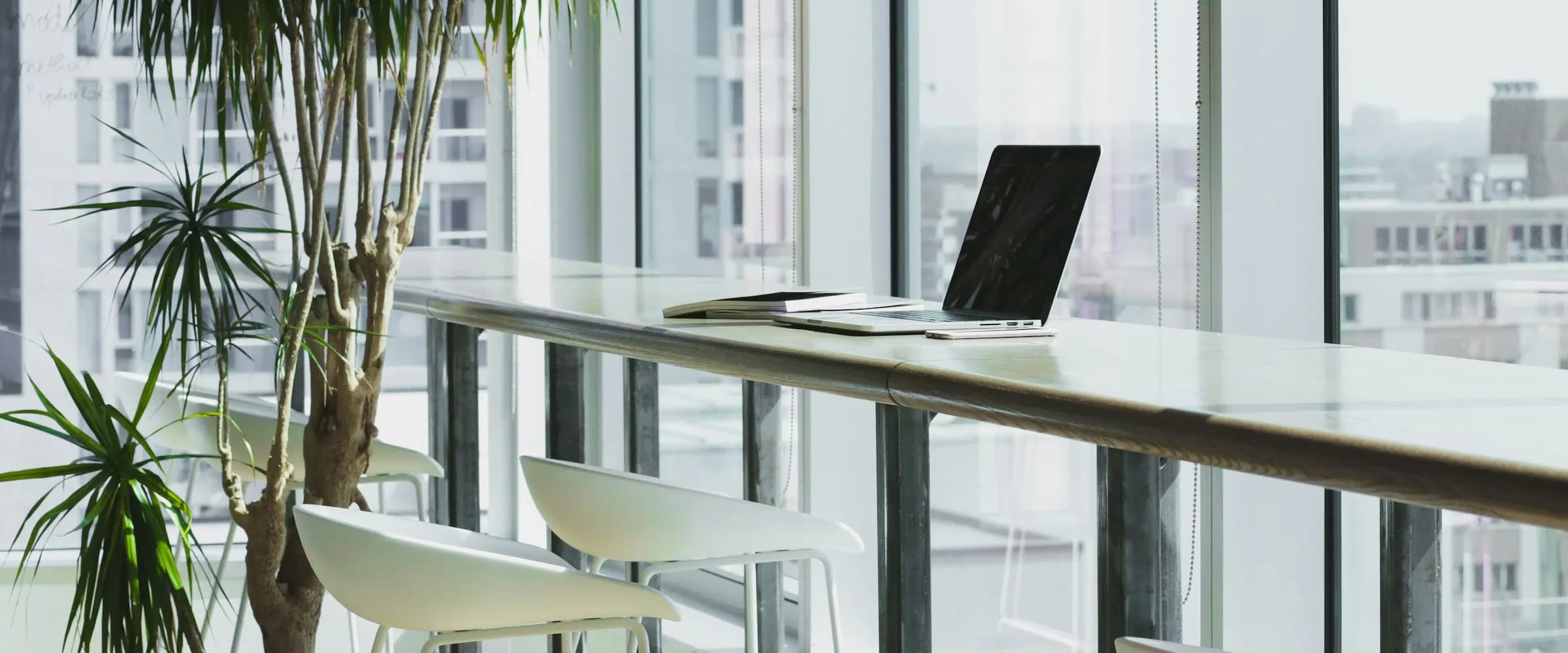 A laptop set up and ready on a long desk by a bright window